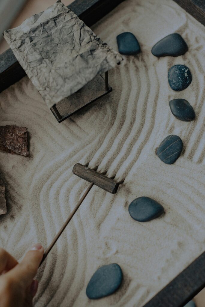 A hand gently guiding a rake through the sand, forming smooth, flowing lines in a Zen garden.