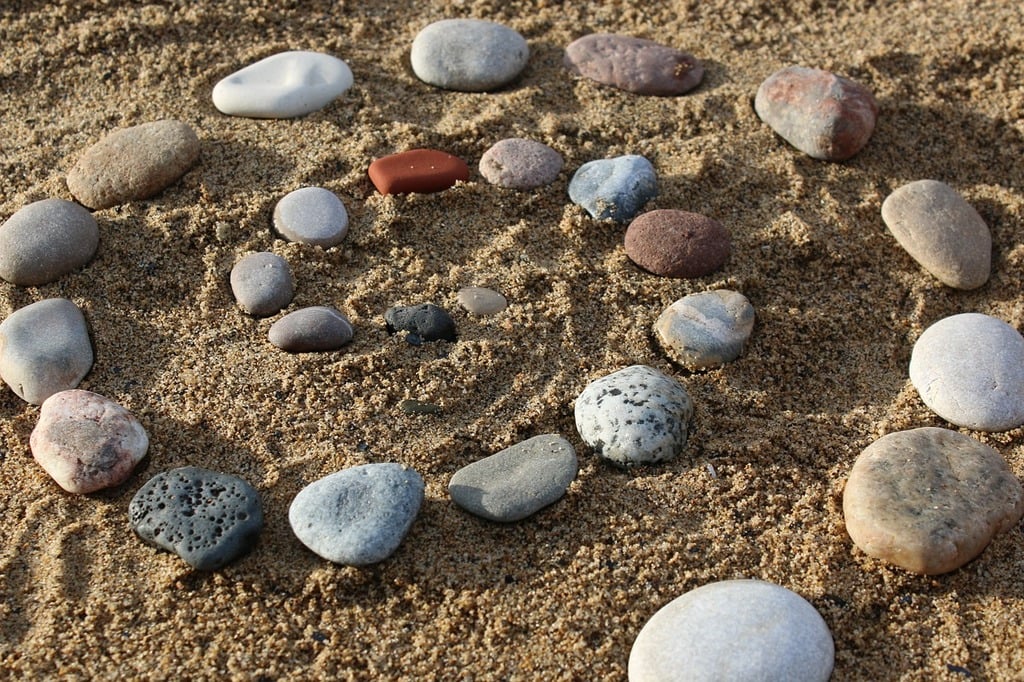 Natural stones are arranged in a spiral pattern in the sand, creating a serene and harmonious Zen garden design. 