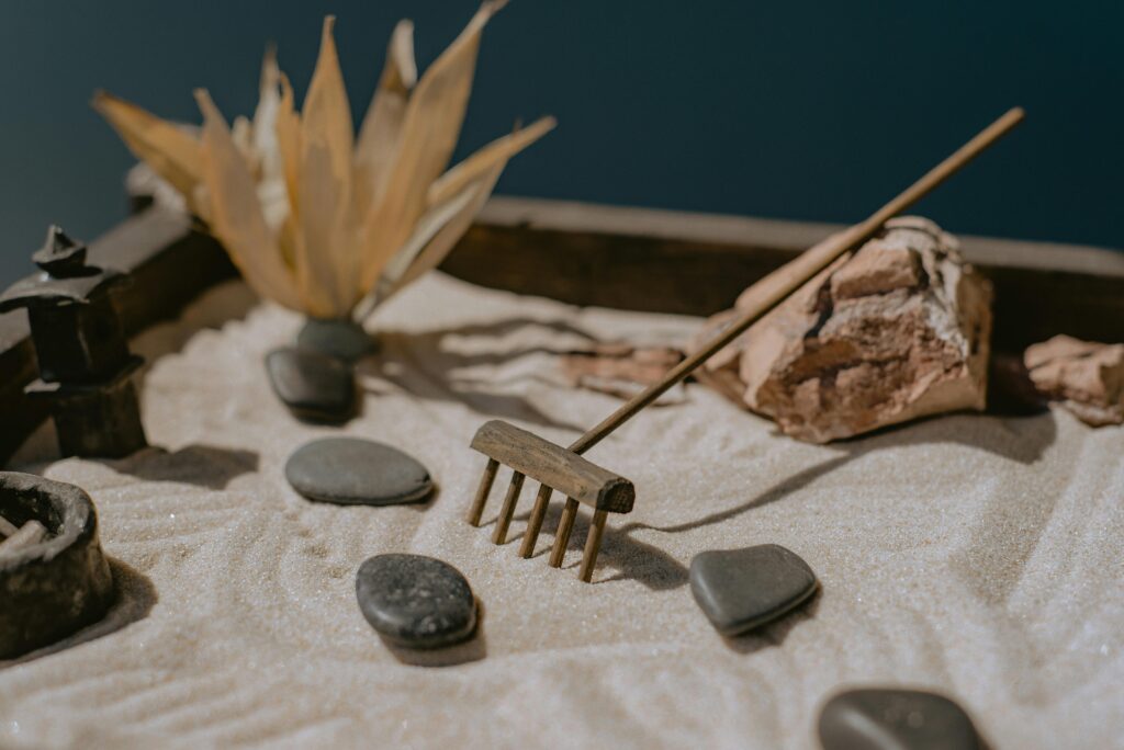 A close-up of a rake creating intricate patterns in the sand of a mini Zen garden.